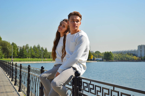Een jong meisje en een jonge man in dezelfde kleren op een brug bij het water. - Foto, afbeelding