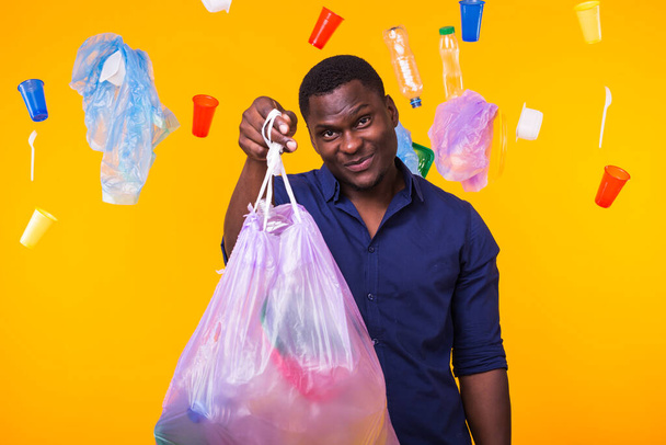 Çöp, plastik geri dönüşüm, kirlilik ve çevre kavramı sorunu - sarı arka planda çöp torbası tutan adam - Fotoğraf, Görsel