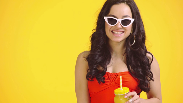 chica feliz con jugo de naranja tocando gafas de sol aisladas en amarillo
 - Metraje, vídeo