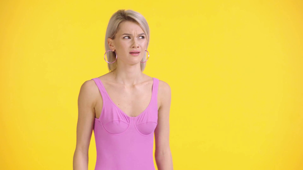 displeased girl in swimsuit showing shrug gesture isolated on yellow - Footage, Video