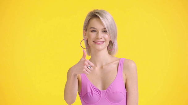 glimlachend meisje in badpak tonen duim omhoog geïsoleerd op geel - Video
