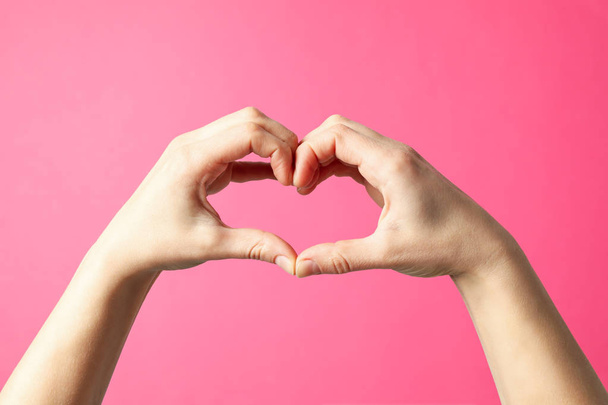 Woman holds hands in the shape of a heart on pink background - Φωτογραφία, εικόνα