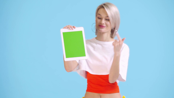 smiling girl showing digital tablet with green screen isolated on blue - Filmati, video