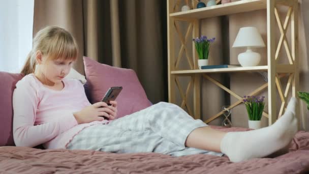 Blonde girl in her bed uses a smartphone - Materiał filmowy, wideo