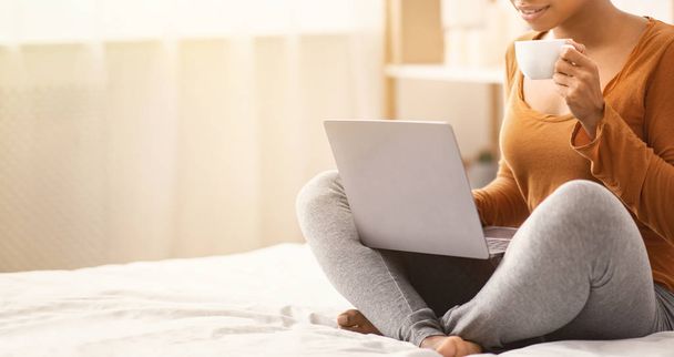 Невизначена чорна жінка використовує ноутбук має ранкову каву в ліжку
 - Фото, зображення