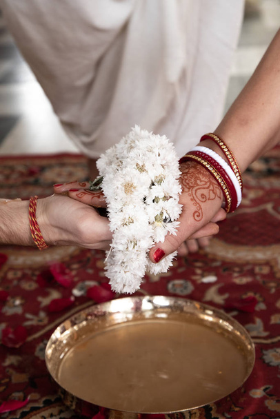 Indian traditional wedding. authentic Vedic wedding ritual called vivaha Yajna. Red Sari, women hands with mehendi close-up. garlands of flowers. Sacred fire ritual. multinational couple. - Valokuva, kuva