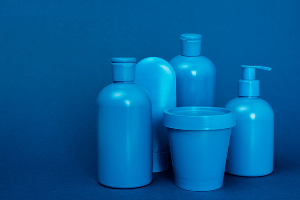 bottles with hair conditioner, shampoo, shower gel, liquid soap and bucket on blue background - 写真・画像