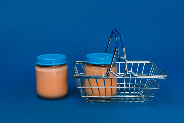 jars with baby food and shopping basket on blue background  - Fotó, kép