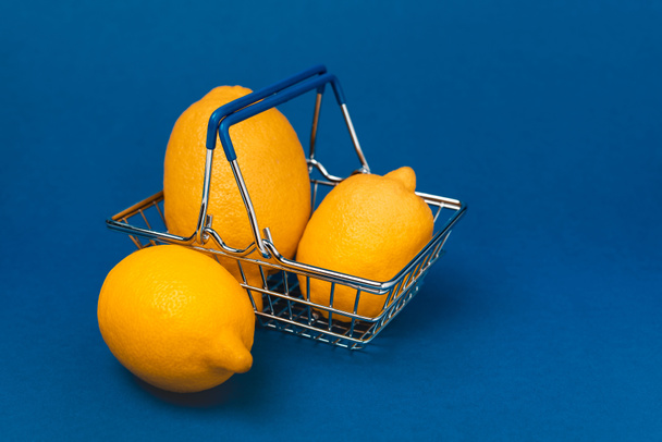 shopping basket with whole and organic lemons on blue background  - Foto, afbeelding
