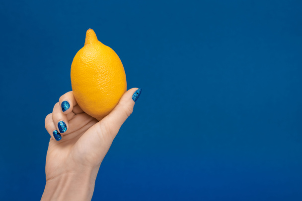 vue recadrée de la femme tenant le citron entier isolé sur bleu
 - Photo, image