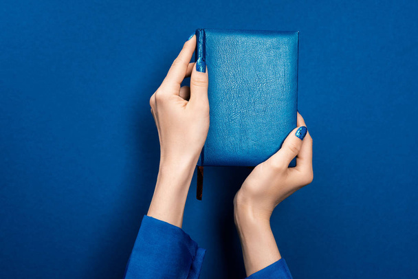 περικοπή άποψη της γυναίκας κρατώντας σημειωματάριο σε μπλε φόντο  - Φωτογραφία, εικόνα