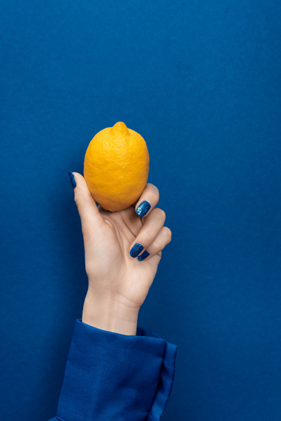 cropped view of woman holding lemon on blue background  - Foto, Bild