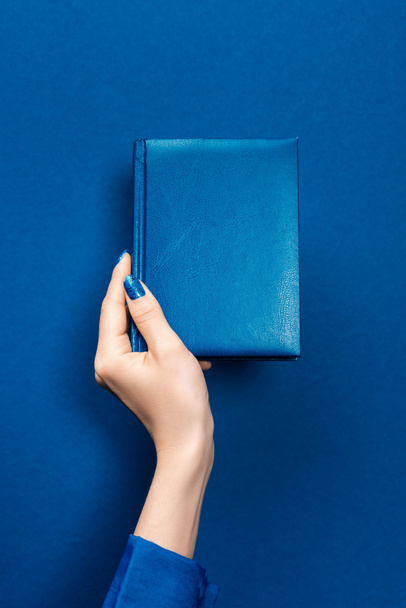 περικοπή άποψη της γυναίκας κρατώντας σημειωματάριο σε μπλε φόντο  - Φωτογραφία, εικόνα