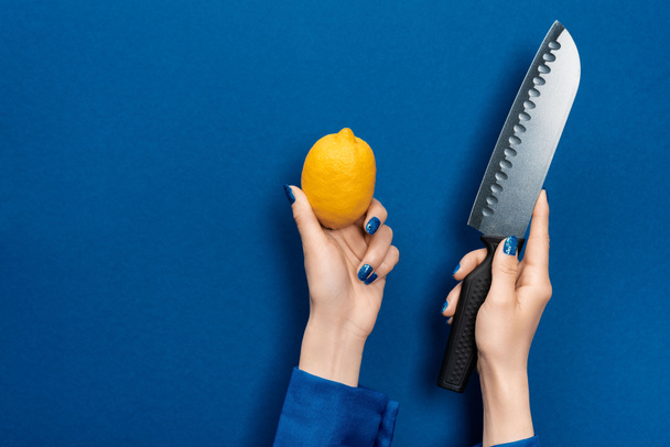cropped view of woman holding lemon and knife on blue background  - Valokuva, kuva