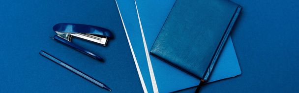 plano panorámico de cuadernos, bolígrafo y grapadora aislados en azul
 - Foto, imagen