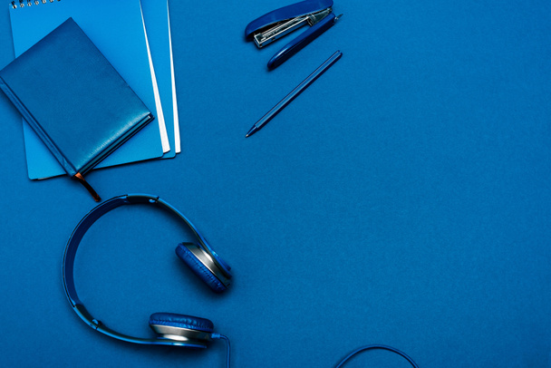 vista dall'alto di notebook, cuffie, penna, cucitrice su sfondo blu
  - Foto, immagini