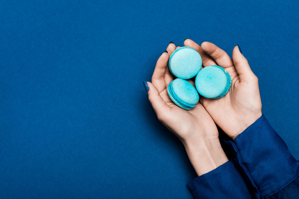 cropped view of woman holding french macaroons on blue background  - Photo, Image