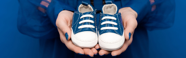 plan panoramique de femme tenant des chaussures de bébé isolées sur bleu
  - Photo, image