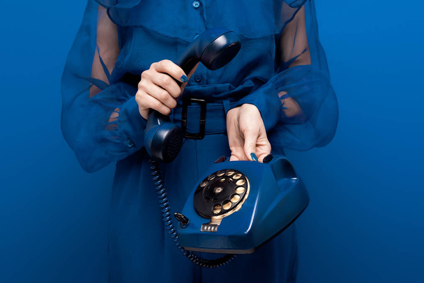 青い背景にレトロな電話を持つ女性の切り取られた眺め   - 写真・画像