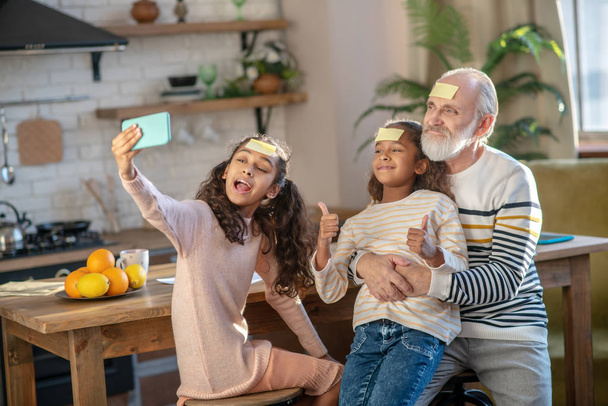 Grey-haired bearded man and his granddaughters looking cheerful - Photo, Image