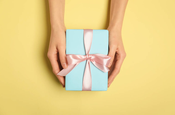 weibliche Hände mit schöner Geschenkbox auf farbigem Hintergrund - Foto, Bild