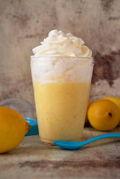 Mousse de limón con crema batida en un vaso transparente, limones frescos sobre un fondo gris. Foto vertical
. - Foto, imagen