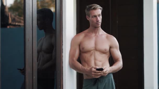 Portrait of sexy muscular shirtless man uses mobile, touches screen with fingers - Video, Çekim