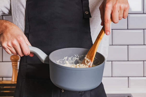 Mans hands close-up holding a saucepan and stirring with wooden spoon. - Photo, Image