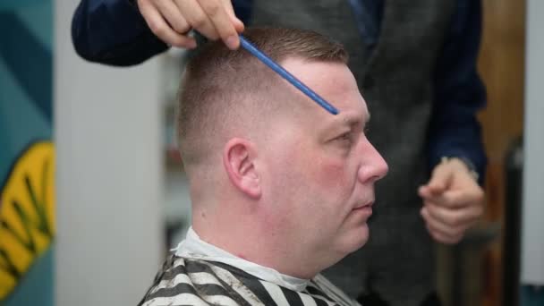 Mens haircut in Barbershop. Close-up of master clipping a man with blond hair with clipper - Materiał filmowy, wideo