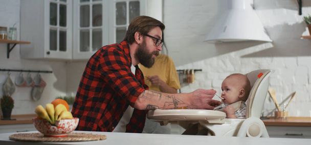 Молодая пара кормит своего ребенка на кухне
 - Фото, изображение