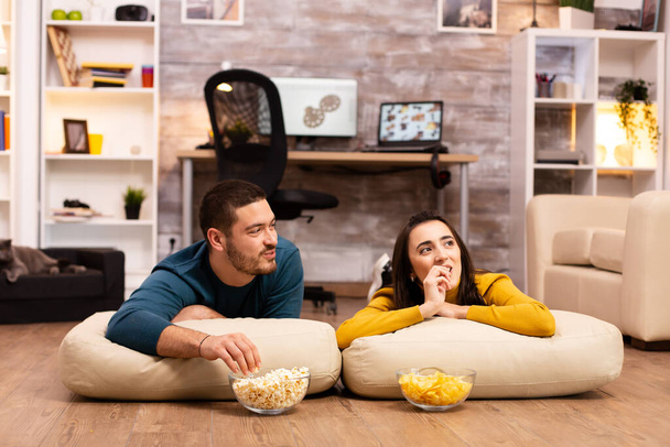 Couple sitting on the floor and watching TV in their living room - Foto, afbeelding
