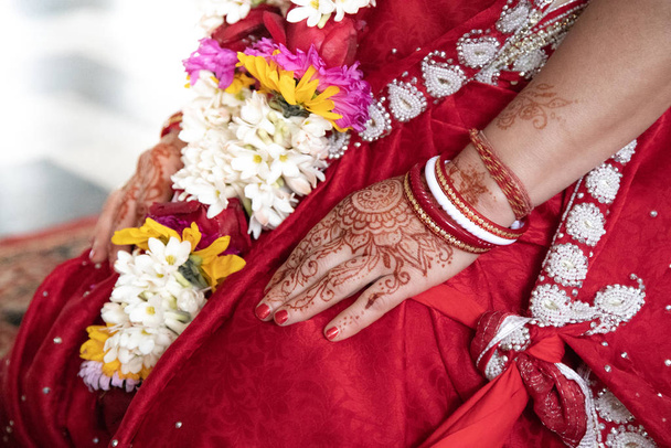 Indian traditional wedding. authentic Vedic wedding ritual called vivaha Yajna. Red Sari, women hands with mehendi close-up. garlands of flowers. Sacred fire ritual. multinational couple - Photo, Image