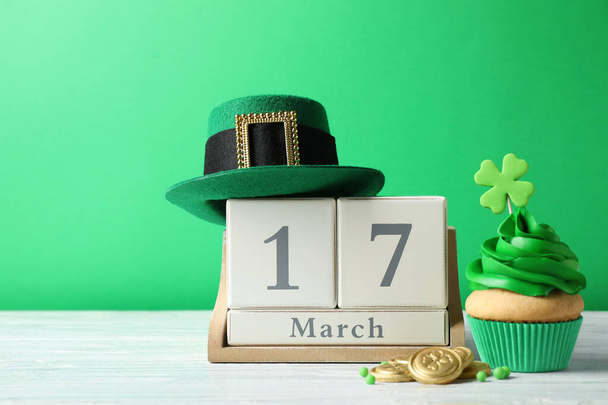 Decorated cupcake, wooden block calendar, hat and coins on white table. St. Patrick's Day celebration - Фото, изображение