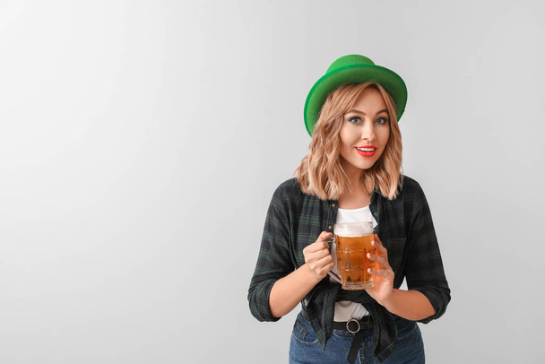 Mooie jonge vrouw met bier op lichte achtergrond. St. Patrick 's Day viering - Foto, afbeelding