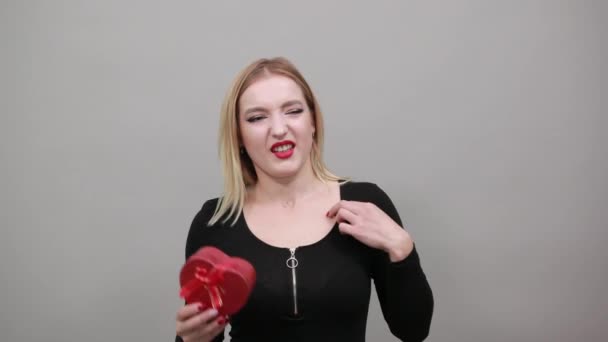 Irritierte Frau hält ein Geschenk in der Hand, rotes Herz, schlechte Laune - Filmmaterial, Video