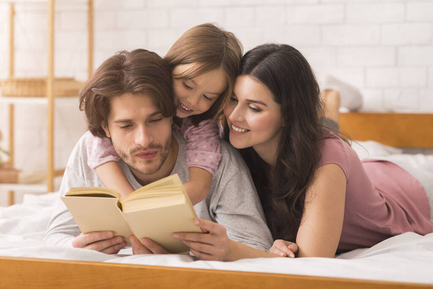 Liebevolle Eltern lesen ihrer kleinen Tochter Märchenbuch vor - Foto, Bild