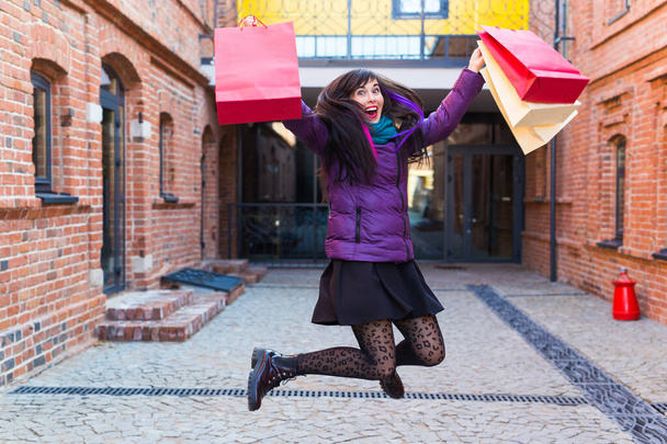 Shopping, concept de consommation et de vente - Drôle de jeune femme sautant avec de nombreux sacs à provisions dans une rue de la ville
 - Photo, image