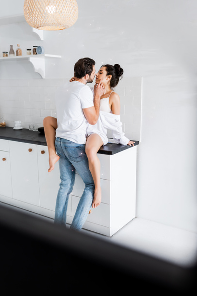 Sütyen ve gömlek giymiş seksi bir kadının mutfak atölyesinde erkek arkadaşını öpmesi.  - Fotoğraf, Görsel