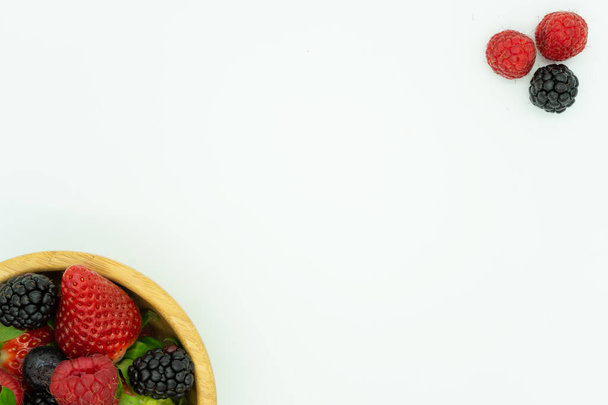 Vista desde arriba de un cuenco de madera lleno de fresas, moras, frambuesas y arándanos. Fondo blanco, espacio para texto. Concepto de comida saludable
. - Foto, Imagen