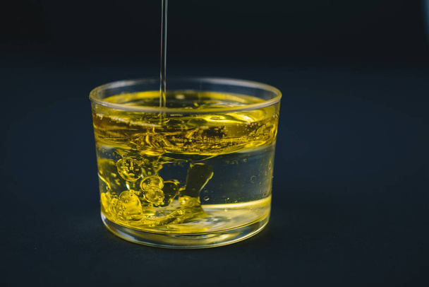 Huile d'olive tombant sur l'eau dans un verre bas avec des gouttes d'huile sur le fond
. - Photo, image