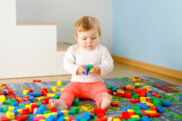 Entzückendes kleines Mädchen, das mit Lernspielzeug spielt. Glückliches gesundes Kind, das mit bunten Holzklötzen zu Hause im häuslichen Raum Spaß hat. Baby lernt Farben und Formen - Foto, Bild