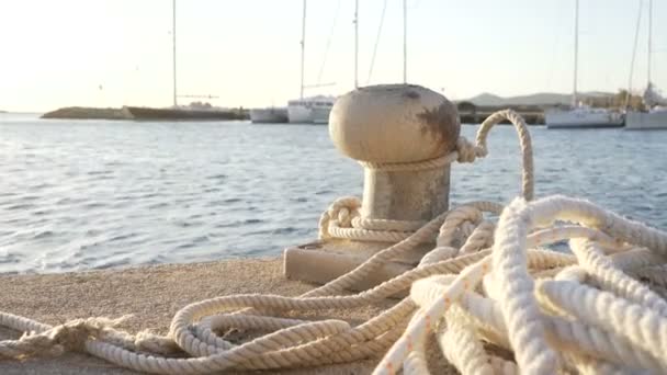 Contre-jour au lever ou au coucher du soleil d'une borne d'amarrage avec la corde attachée et reposant sur le sol et divers bateaux en arrière-plan dans la lumière arrière
 - Séquence, vidéo