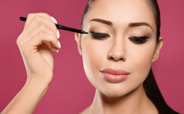 Beautiful woman applying eyeliner on pink background, closeup. S - Foto, immagini