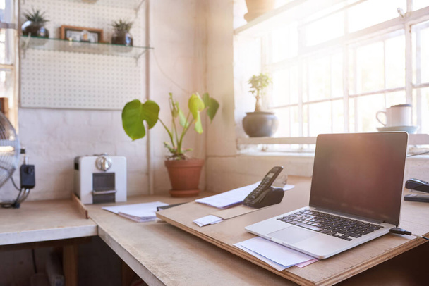 Laptop and other business supplies sitting on a table in the office area of a framing shop, with sun flare behind - 写真・画像