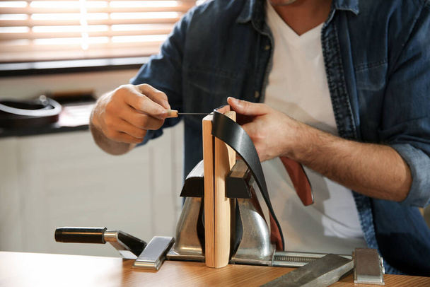 Man making holes in leather belt with stitching awl at table, closeup - Foto, afbeelding