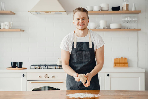 Männlicher Koch Koch Koch Bäcker lächelt, hält frischen Teig in Händen in Schürze, helle Hintergrundküche - Foto, Bild