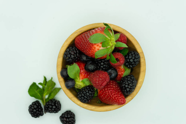Vue du dessus d'un bol en bois rempli de fraises, mûres, framboises et bleuetiers.Fond blanc, espace pour le texte. Concept d'alimentation saine
. - Photo, image