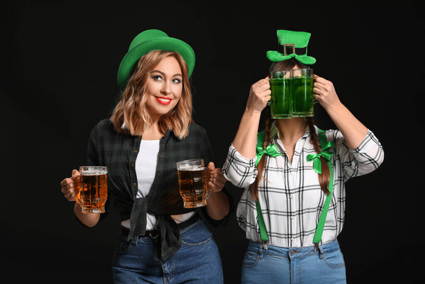 Grappige jonge vrouwen met bier op donkere achtergrond. St. Patrick 's Day viering - Foto, afbeelding