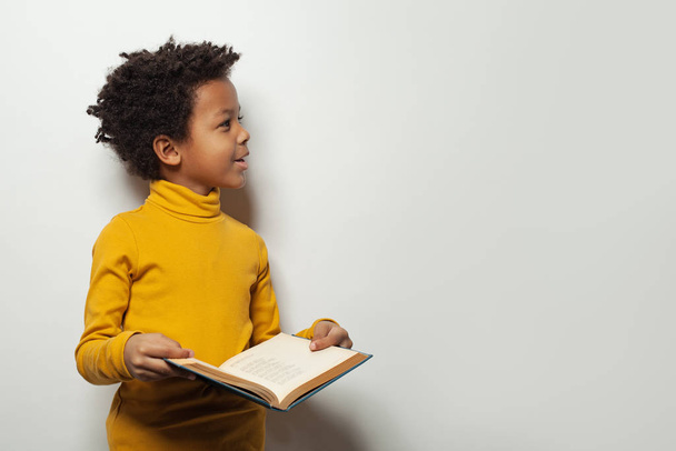 Kíváncsi fekete gyerek fiú olvas egy könyvet a fehér háttér - Fotó, kép