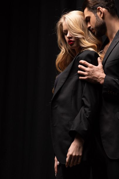 handsome man touching beautiful woman in suit isolated on black  - Valokuva, kuva